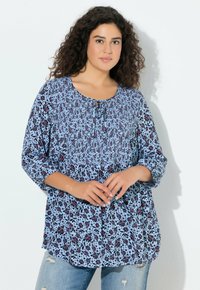 Kwiatowa bluzka w jasnoniebieskim kolorze z czarnymi i czerwonymi wzorami, z okrągłym dekoltem, wiązaniem oraz rękawami do połowy przedramienia.