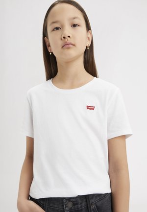 T-shirt bianco in cotone con maniche corte e scollo rotondo. Presenta un piccolo logo rosso "Levi's" sul lato sinistro del petto. Indossato con jeans scuri.