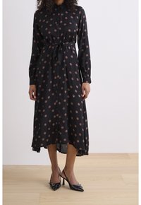 Svart knapp-up klänning med långa ärmar, med ett rosa prickigt mönster och ett knytbälte i midjan. Slät tyg med ett flytande snitt.