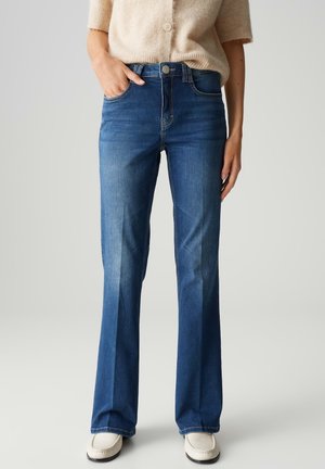 Jean bleu évasé en denim avec un lavage moyen. Les caractéristiques incluent une taille ajustée, deux poches avant et une texture légèrement déchirée.