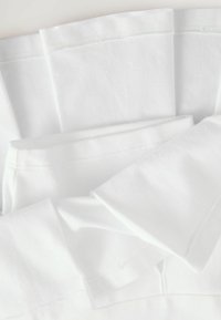 Weiße Baumwoll-T-Shirts sind mit glatten, gefalteten Kanten und kurzen Ärmeln versehen. Sie zeichnet sich durch ein einfaches, nahtloses Design und eine weiche Textur aus.
