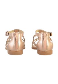 Sandalias de oro rosa con diseño recortado, cremallera trasera y correa para el tobillo. Textura metálica suave con suela plana y mínimos acentos decorativos.