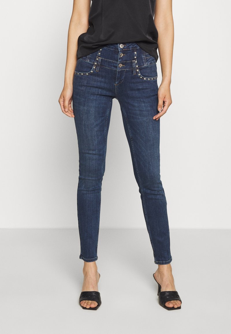Mörkblå skinny jeans med hög midja, prydda med dekorativa fickor och silverfärgade nitar. Slät denim med lite stretch.