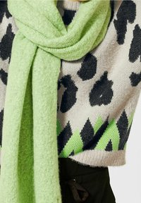 Tröja med svarta leopardfläckar och gröna geometriska accenter, i kombination med en mjuk, ljusgrön scarf i texturerat material.