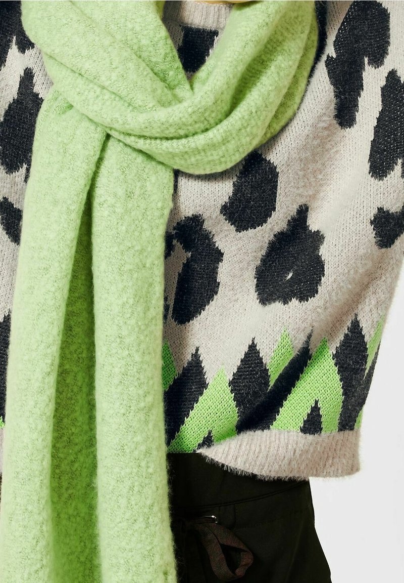 Tröja med svarta leopardfläckar och gröna geometriska accenter, i kombination med en mjuk, ljusgrön scarf i texturerat material.