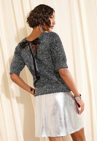 Fekete és ezüst pulóver, texturált felülettel és rövid ujjakkal, hátul masnis részlettel. Fényes ezüst A-vonalú szoknyával párosítva.