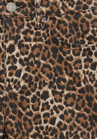 Tissu à imprimé léopard avec des taches marron, noires et beiges ; couture de poche visible et bouton métallique sur un matériau en denim.