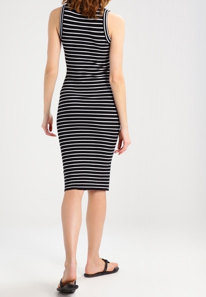 Robe midi sans manches à rayures noires et blanches, silhouette ajustée et texture côtelée. Le modèle porte des sandales plates noires.