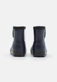 Une paire de bottes de pluie en caoutchouc bleu marine avec des semelles noires et des bordures noires, vue de l'arrière sur un fond blanc.