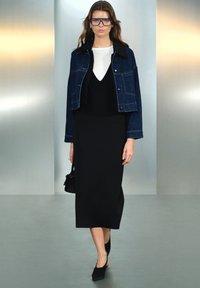 Chaqueta de mezclilla corta, top blanco con escote en V, falda negra ajustada, zuecos negros, bolso negro pequeño, gafas de marco transparente. Texturas suaves.