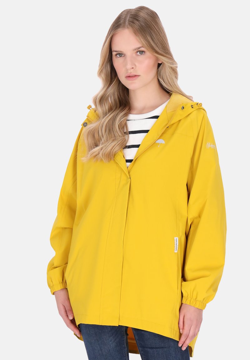 Sárga vízálló kapucnis dzseki, gumis mandzsettával és egyenes szabással. Alatta fehér csíkos ing van.