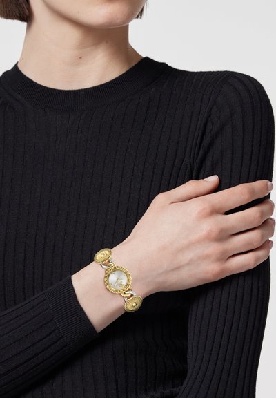 Kuldne metall käekell ümmarguse sihverplaadiga ja dekoratiivsete ümmarguste linkidega, millel on hõbedane kellaplaat ja keerukad detailid.