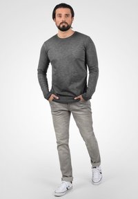 Grå langærmet skjorte med en blød tekstur, parret med lysegrå jeans og hvide sneakers. Enkel, afslappet stil med en løs pasform.