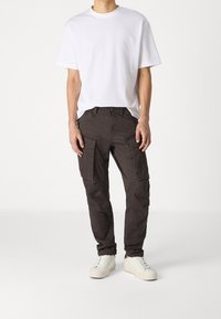 Donker cargobroek met meerdere zakken, gemaakt van katoen, gecombineerd met een eenvoudige witte T-shirt met ronde hals. Schoeisel zijn lichte sneakers.