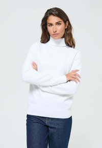 Pull à col roulé blanc avec une texture douce et une coupe décontractée, doté de poignets et d'un ourlet côtelés, associé à un jean bleu foncé.