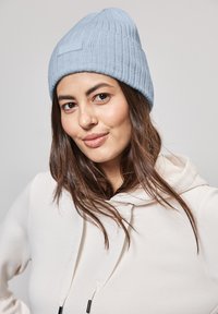 Ljusblå stickad mössa med ribbad textur och en liten etikett. Bärs med en krämfärgad hoodie som har dragsnören med svarta accenter.