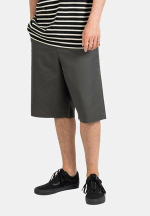 Dark green shorts made from a lightweight fabric, featuring a straight cut and knee-length design, paired with black suede sneakers.