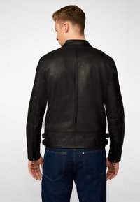 Zwarte leren jas met een soepele textuur, voorzien van een bandkraag en verstelbare bandjes bij de taille. Strak aansluitend ontwerp, gecombineerd met donkere jeans.