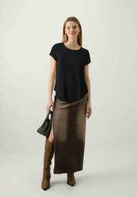 Czarny krótki top noszony z maxi spódnicą w brązowym gradientzie. Modelka trzyma torebkę z teksturowanego czarnego materiału i ma na sobie wysokie brązowe botki.