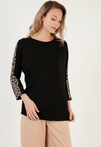 Black top with three-quarter leopard print sleeves. Soft fabric, round neckline, relaxed fit, detailed accents add contrast to the simple design.