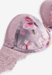 Biustonosz z koronki i satyny w jasnofioletowym kolorze z miseczkami w kwiatowy wzór. Charakterystyczne koronki zdobiące pas oraz gładka faktura miseczek.