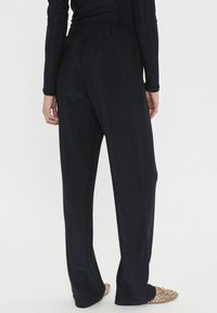 Crne, rastezljive hlače s labavim krojem, s mekim sjajem i elastičnom pričvršćenom trakom. Glatka tekstura, dizajn do poda, uparen s ravnim cipelama.