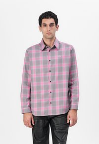 Camisa de manga larga, abotonada en gris con un patrón de cuadros en rosa. Presenta un collar puntiagudo y un pequeño logo en el pecho. Textura suave.