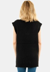 Svart stickad ärmlös tunika med ribbad textur, som har en avslappnad passform och sidokilar, ihop med åtsittande blå jeans.