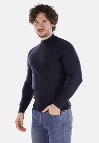 Maglione aderente blu navy in un tessuto a maglia liscia, con collo alto e maniche lunghe, abbinato a jeans blu chiaro.