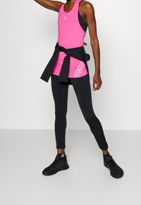 Vaateet: vaaleanpunainen urheilupaita mustan pitkähihasen päällä, yhdistettynä mustiin legginsseihin ja mustiin urheilukenkäisiin, joissa on valkoisia yksityiskohtia.