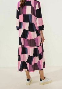 Barevné vrstvené šaty s velkými geometrickými vzory v růžové, černé a námořnické modři, vyrobené z měkké látky, s tříčtvrtečními rukávy.