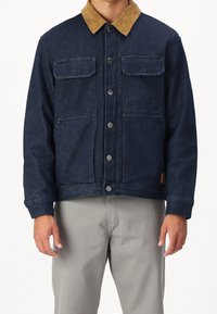 Tummansininen farkkutakki, jossa on vaaleanruskea samettikaulus, napit edessä ja kaksi rintataskua. Takissa on rento leikkaus ja teksturoitu kangas.