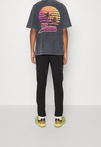 Svarta cargobyxor kombinerade med en urtvättad svart t-shirt med en färgstark solnedgång och palmer. Skorna är gula med svarta detaljer.