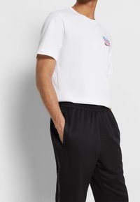 Vit bomullströja med korta ärmar och en f ärgglad grafik på vänster bröst, i kombination med svarta joggerbyxor med elastisk midja.