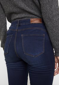 Mörkblå denimjeans med en figurnära design, med bakfickor, kontrasterande bruna sömmar och en brunt läderetikett i midjan.