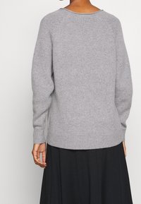 Harmaa neulepaita, jossa on pitkät hihat, pyöreä kaula-aukko, ribbaustekniikalla tehdyt hihansuut ja helma, sekä pehmeä rakenne, nähtynä takaa.