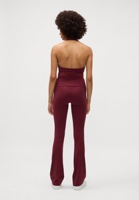 Macacão sem mangas cor bordô com corpete ajustado e calças flare, feito de tecido suave, com um design traseiro elegante e sem fechos visíveis.