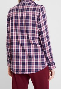 Mörkblå och rosa rutig skjorta med långa ärmar, knäppningsmanchetter och klassisk krage. Har en rak nederkant och detalj vid ryggen.