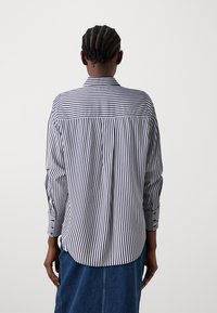 Camicia a righe in tessuto blu navy e bianco, con colletto classico, maniche lunghe e orlo curvato, caratterizzata da un design a vestibilità rilassata.