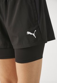 Pantalones cortos deportivos negros fabricados en tejido ligero, con un panel de malla y un logo blanco de Puma en el lado. Incluye pantalones cortos ajustados negros.