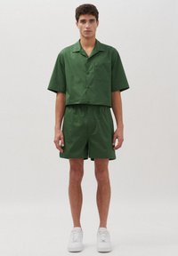 Camicetta verde a maniche corte e pantaloni coordinati realizzati in un materiale morbido e leggero. Presenta una tasca sul petto e una cintura elasticizzata.