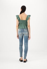 Top peplum verde con smock y mangas acampanadas, combinado con jeans ajustados azul claro. Tejido texturizado con detalles de patrón sutil.