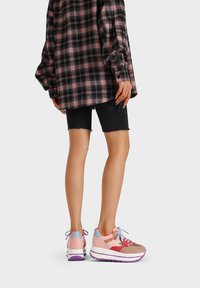 Sneakers multicolori in suede rosa, rossa e beige, con suola chunky bianca e viola, abbinate a pantaloni shorts di denim neri e una camicia a quadri.