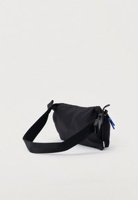 Μαύρη νάιλον τσάντα με μαλακή, στρογγυλή μορφή, ρυθμιζόμενο λουρί και κλεισίματα με φερμουάρ, με μπλε λεπτομέρειες και κομψή υφή.