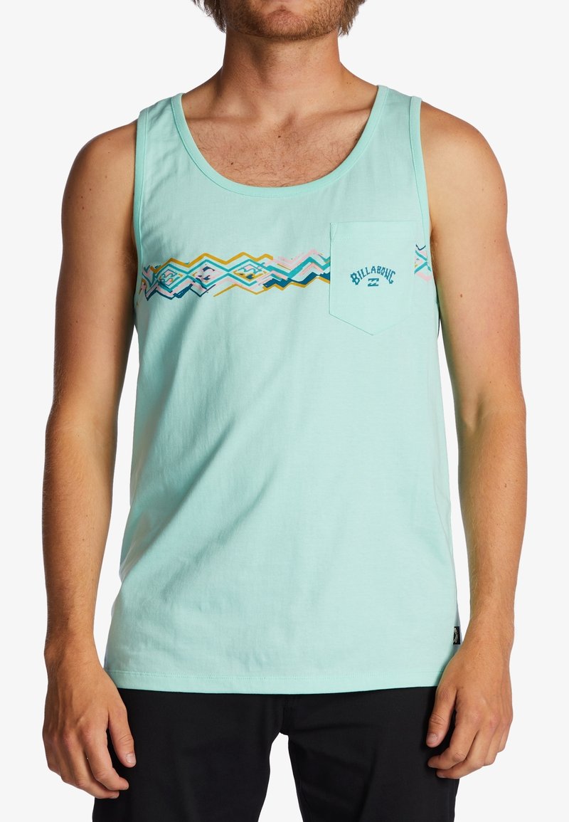Homme portant un débardeur bleu clair à motif géométrique avec le logo Billabong sur la poche poitrine, associé à un short noir.