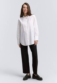 White button-up shirt with a pointed collar, long sleeves, and a relaxed fit, paired with black tapered pants and black shoes.