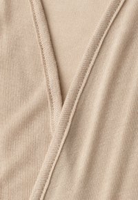 Detailní záběr béžové pletené látky, ukazující podrobnou texturu a překrývající se složené okraje.