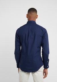 Mörkblå långärmad skjorta med en strukturerad krage, knappmanschetter och rak nederkant. Tillverkad av en slät tyg, har en ryggfälld som ger bättre passform.