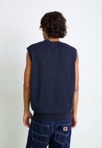 Jersey de punto sin mangas en color marino con cuello y bajo acanalados, hecho de un material texturizado, combinado con pantalones cargo azul oscuro que cuentan con un parche.