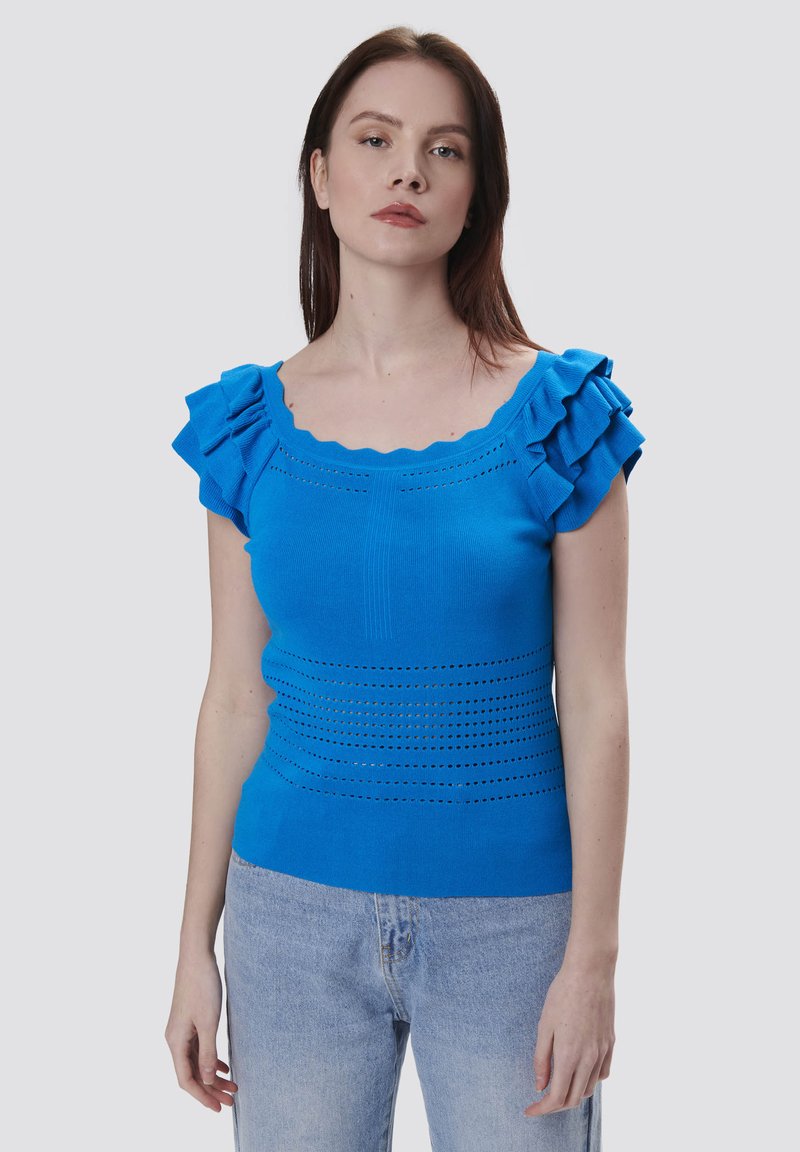 Blaues gestricktes Oberteil mit Rüschensleeves, wellenförmigem Ausschnitt und strukturierten horizontalen Linien mit offenen Details. Kombiniert mit hellblauen Jeans.